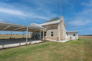 A stone house with a covered porch and a small adjacent structure. - Historic 1800s Rock House w/ horse corral (Gatesville)