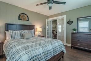 A bedroom with a bed, a nightstand, a dresser, a ceiling fan, and a door leading to a dining area. - Historic 1800s Rock House w/ horse corral (Gatesville)