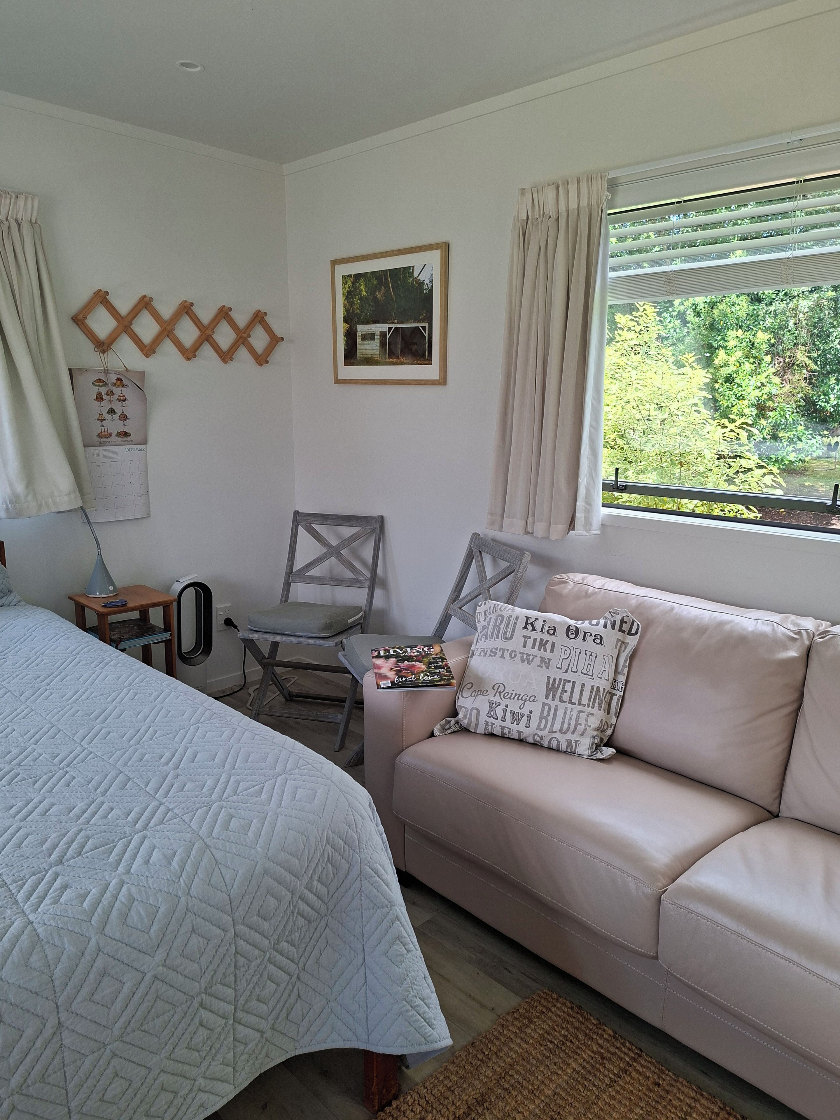 Une chambre à coucher comprenant un lit, un canapé, un fauteuil, un calendrier et une fenêtre donnant sur un paysage verdoyant.