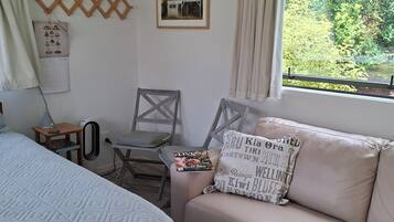 A bedroom with a bed, a sofa, a chair, a calendar, and a window with a view of greenery.