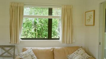 A room with a beige sofa, two pillows with text, a window with curtains, and a framed picture on the wall.