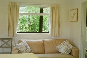 A room with a beige sofa, two pillows with text, a window with curtains, and a framed picture on the wall.