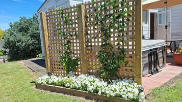 A wooden lattice structure with climbing plants and white flowers, a patio area with a table and chairs, and a white building in the background.
