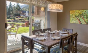 A dining area with a table set for four, a grill outside, and a view of a garden and mountains. - Spacious  2-bedroom condo with AC and fireplace in beautiful Leavenworth (Leavenworth)