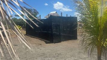 Una estructura negra con una puerta, rodeada de palmeras y un cielo despejado.