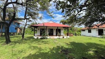 Una casa de techo rojo, rodeada de un césped cuidado y árboles.