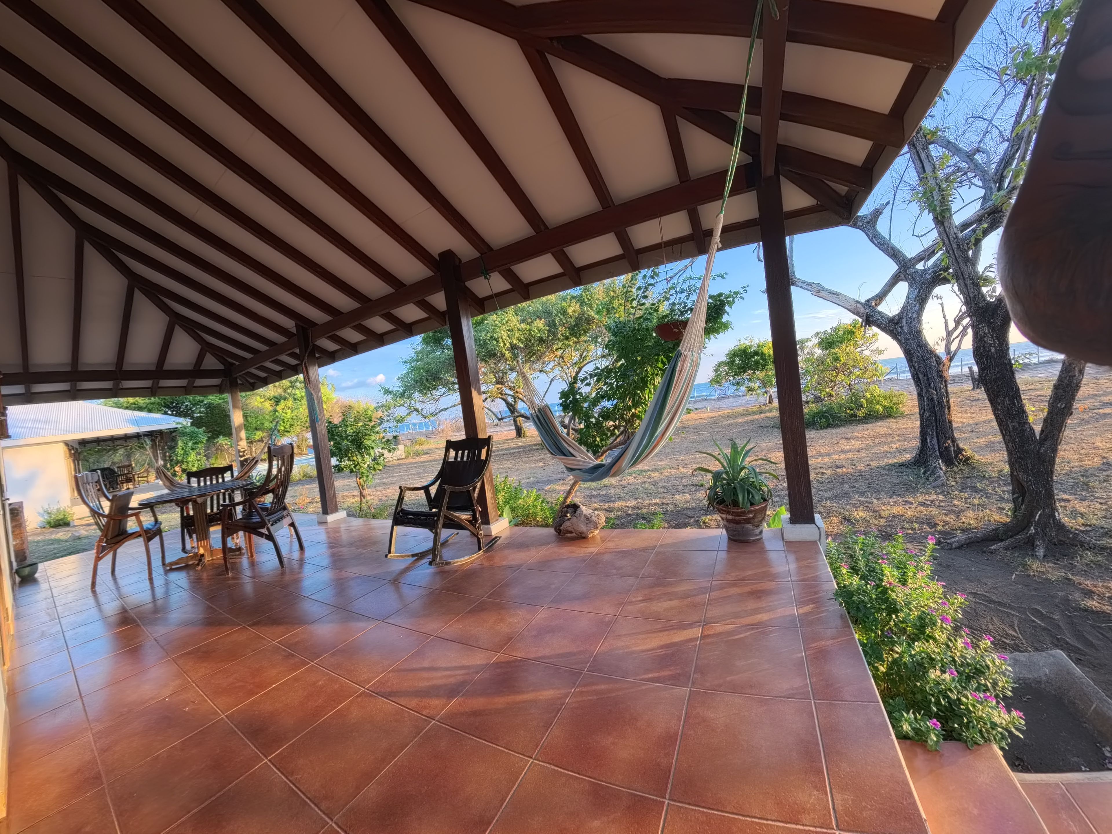 A covered patio with a tiled floor, outdoor furniture, and a hammock.