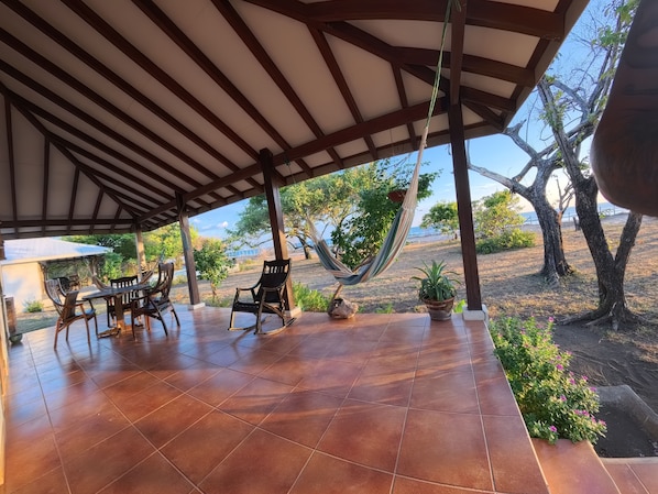 A covered patio with a tiled floor, outdoor furniture, and a hammock.