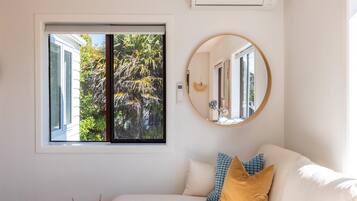 A room with a white couch, a round mirror, and a window with a view of greenery.