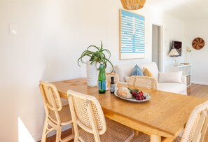 A dining area with a wooden table, wicker chairs, a white sofa, and a wall-mounted painting.