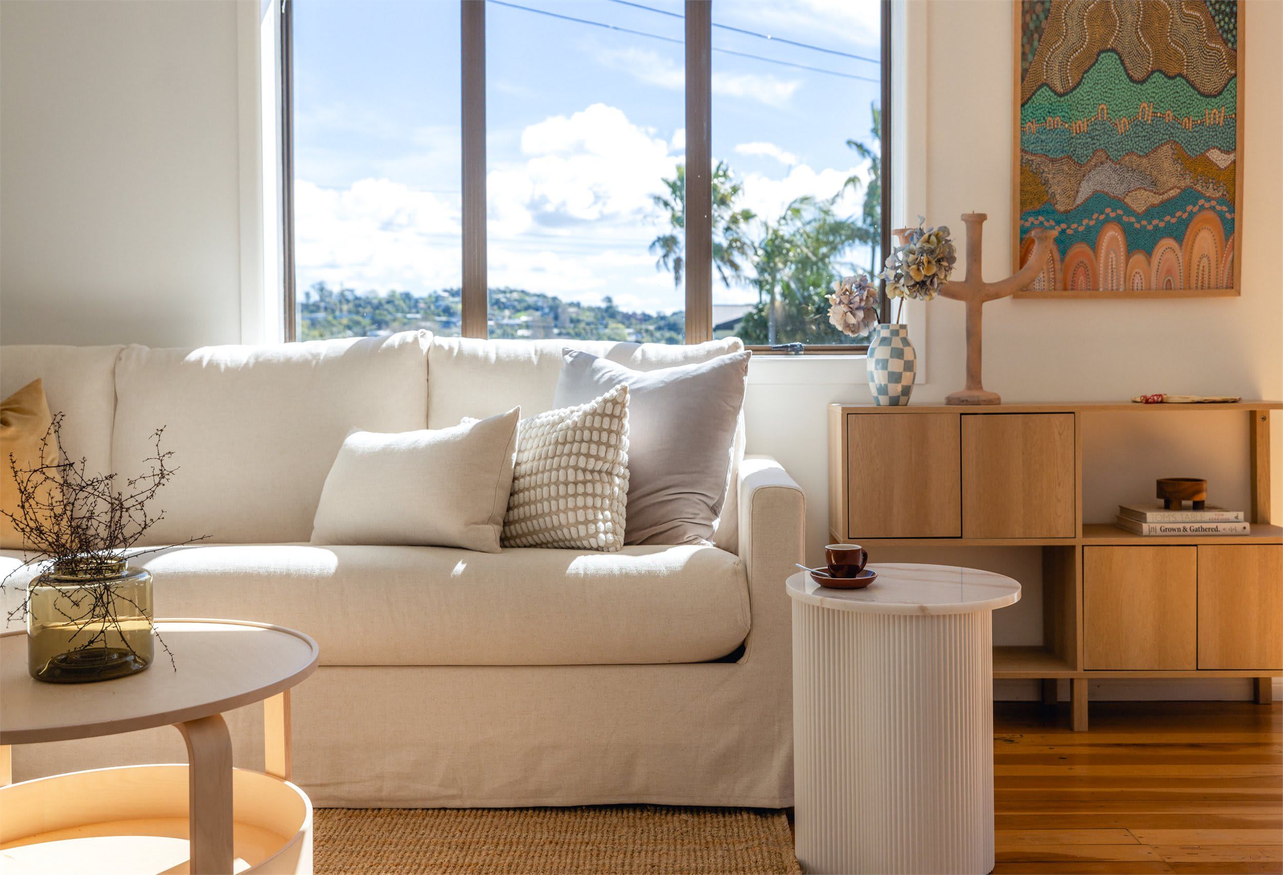 A modern living room with a sofa, a round side table, a cabinet, and a painting on the wall.