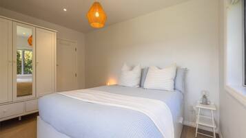 A bedroom with a bed, a wardrobe, a bedside table, and a hanging light fixture.