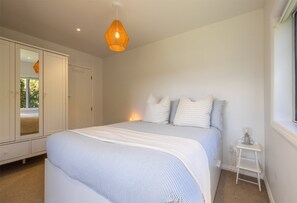 A bedroom with a bed, a wardrobe, a bedside table, and a hanging light fixture.