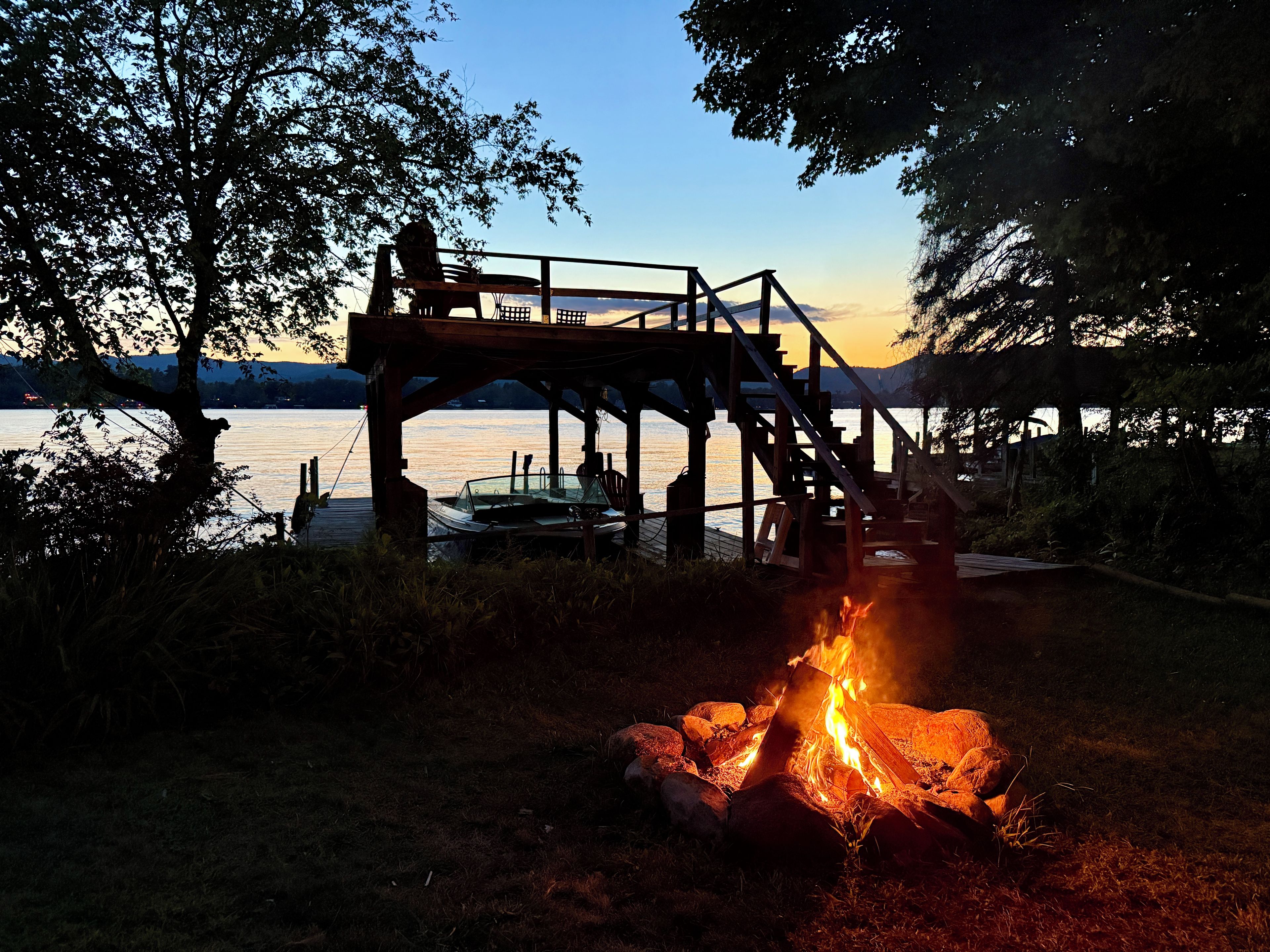 A wooden deck overlooking a lake with a fire pit in the foreground.