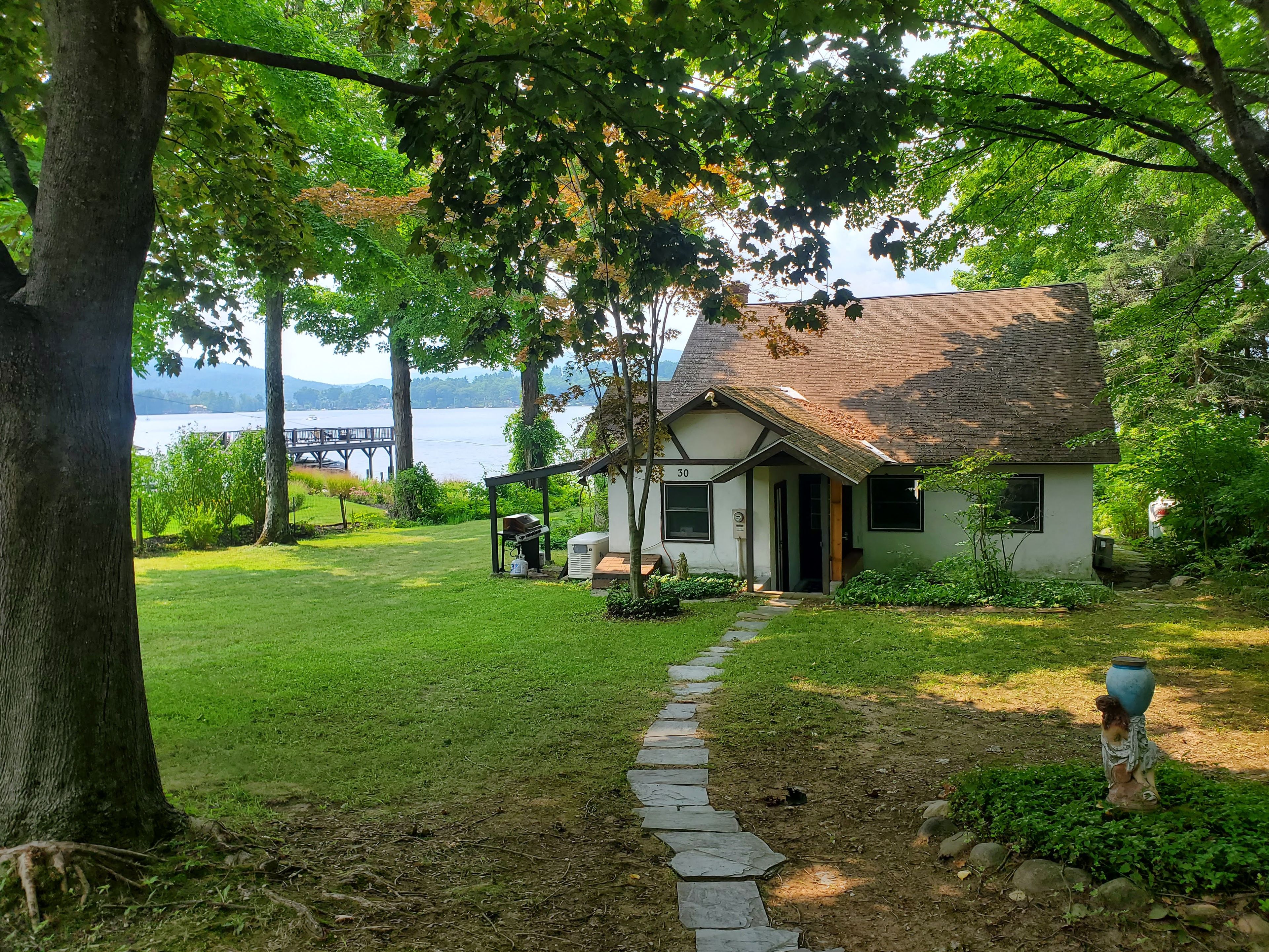 Una casa con un camino de piedra que conduce a la puerta principal, rodeada de abundante vegetación y vistas a un lago.