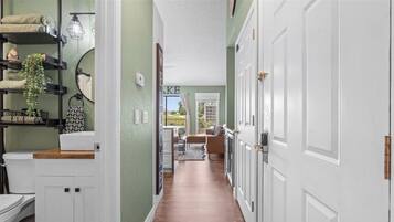 A hallway with a white door, a welcome sign, and a view into a living area with a rug and furniture.