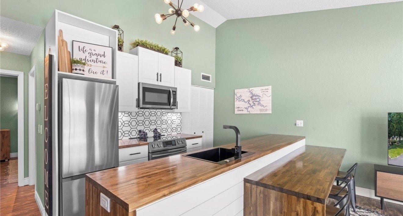 A modern kitchen with a stainless steel refrigerator, microwave, and stove, a wooden countertop, and a sink.