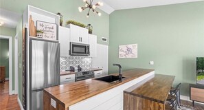 Cozinha moderna com geladeira de aço inoxidável, micro-ondas e fogão, bancada de madeira e pia.