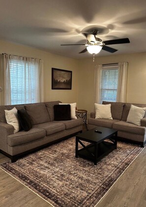 A living room with two sofas, a coffee table, a ceiling fan, and a framed picture on the wall. - Cozy 2-bedroom house in nice Travelers Rest with AC (Travelers Rest)