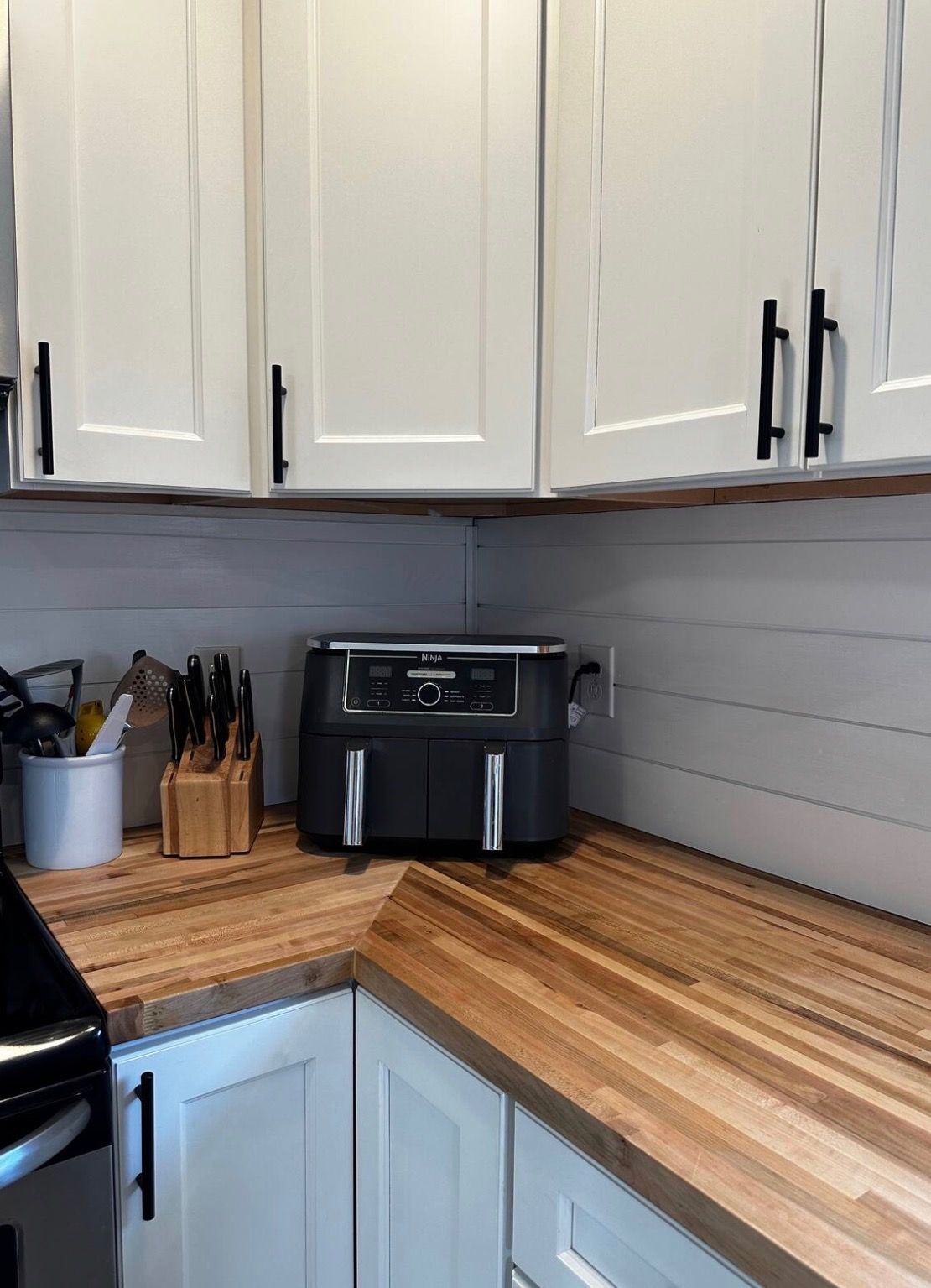A kitchen with white cabinets, a black appliance, and a wooden countertop.
