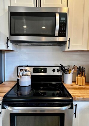 A kitchen with a stainless steel microwave, a kettle, and a stove.