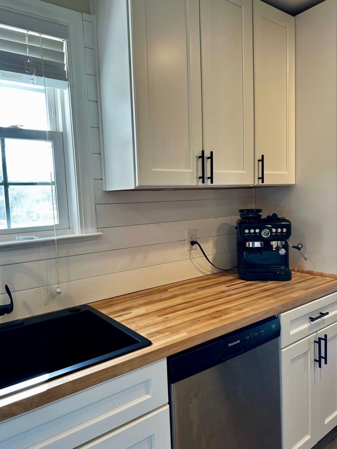 A kitchen with white cabinets, a wooden countertop, a built-in dishwasher, and a coffee maker.