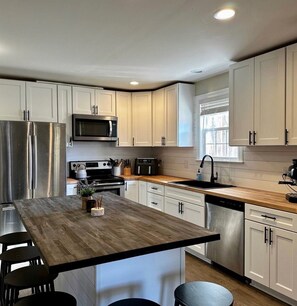 A modern kitchen with white cabinets, stainless steel appliances, and a wooden island. - Cozy 2-bedroom house in nice Travelers Rest with AC (Travelers Rest)