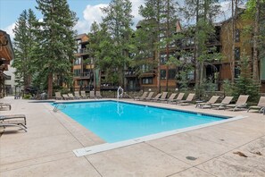 A swimming pool with lounge chairs and a wooden building with balconies. - Lances West 9: Cozy condo with easy access to the slopes and town! (Breckenridge)