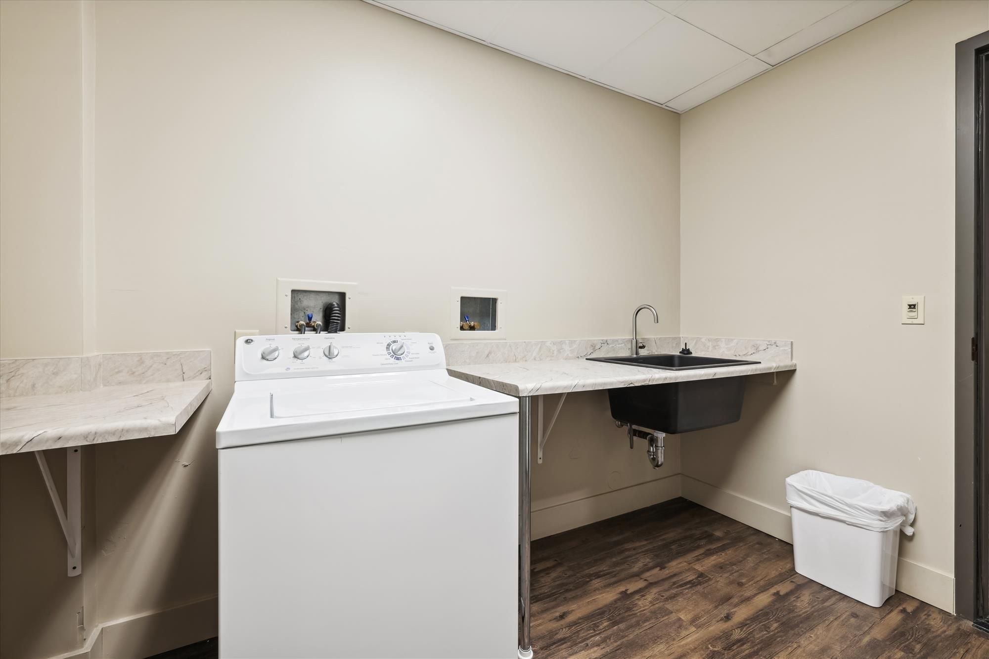 A laundry area with a washing machine, a sink, and a trash bin.