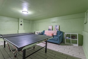 A room with a ping pong table, a blue sofa, and a white shelf with books. - Bear Basecamp/3BR/Game Room/Midterm Welcome (Waco)