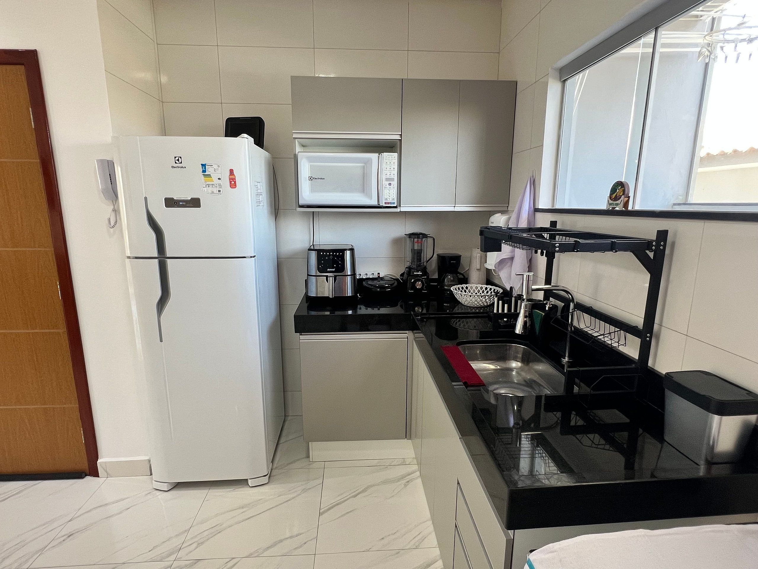 A compact kitchen with a refrigerator, microwave, coffee maker, and a sink with a drying rack.