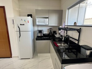 A compact kitchen with a refrigerator, microwave, coffee maker, and a sink with a drying rack. - Capitania Residence (Porto Seguro)