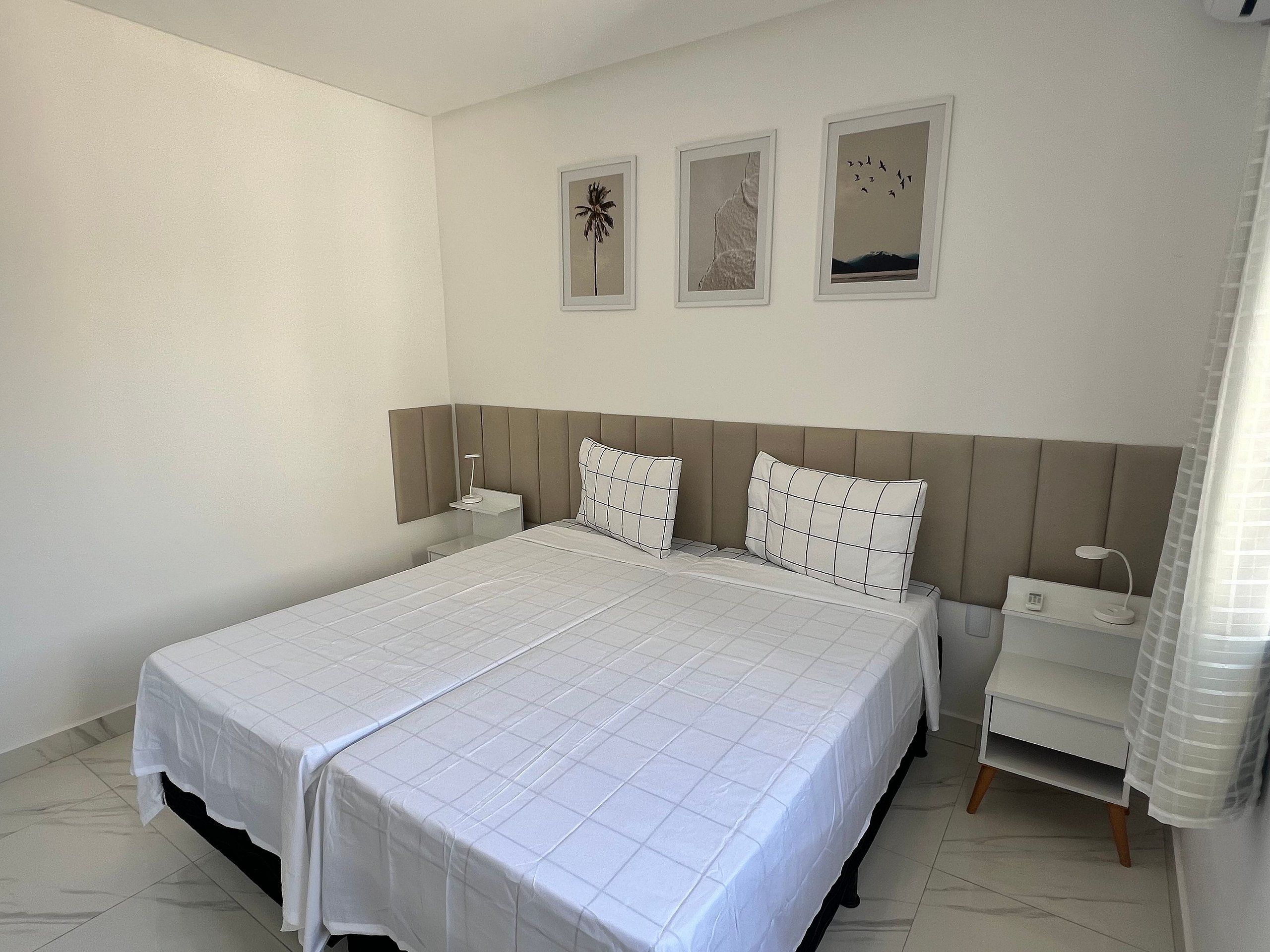 Una habitación de hotel con una cama grande, dos mesitas de noche y tres cuadros enmarcados en la pared.