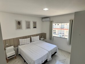 A hotel room with a bed, bedside tables, a window with curtains, and wall art.