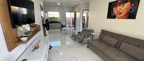 Una sala de estar moderna con un televisor de pantalla plana grande, un sofá, un comedor y una cocina al fondo.
