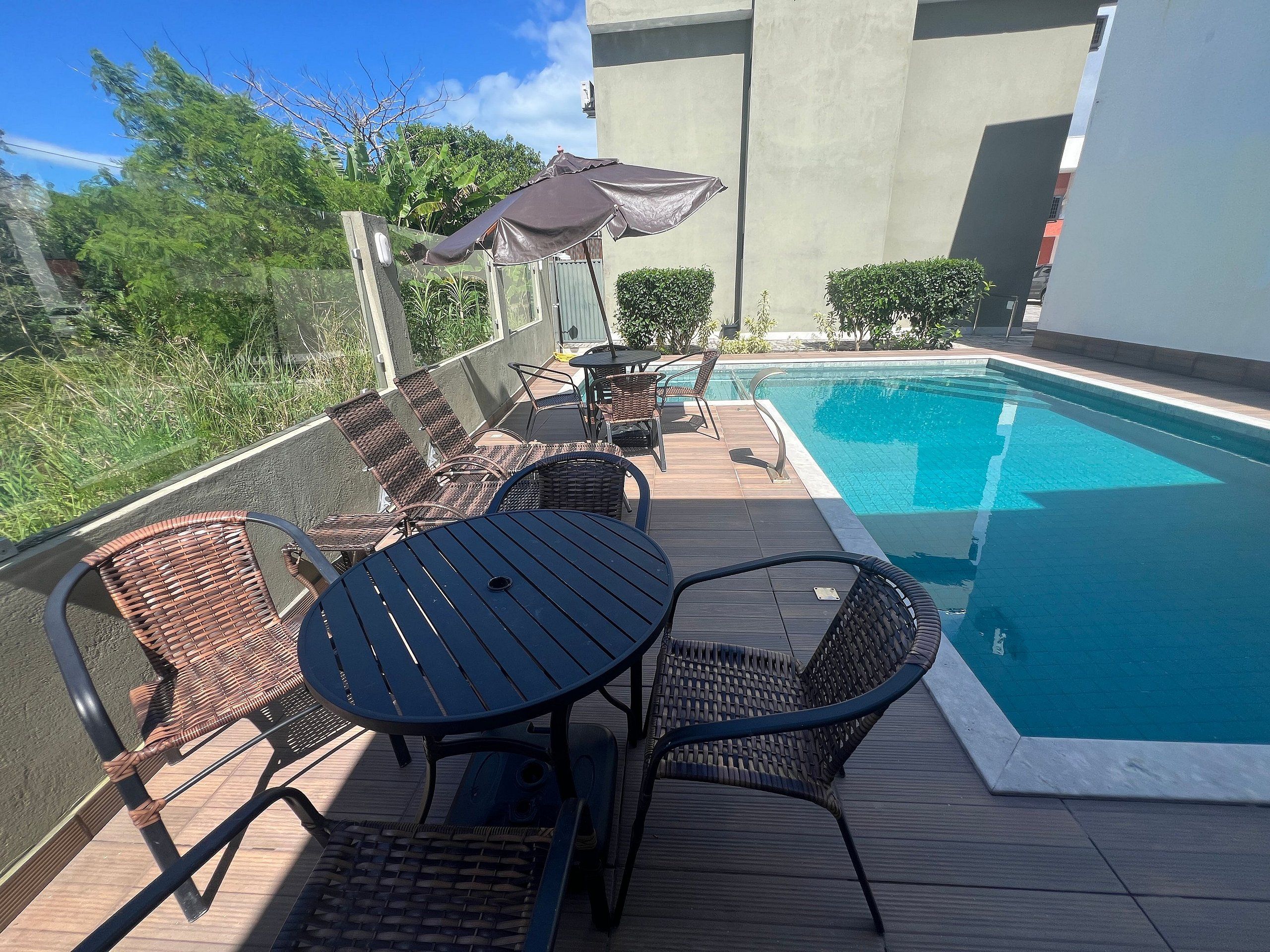 A poolside area with a table and chairs, a small umbrella, and a view of the pool.