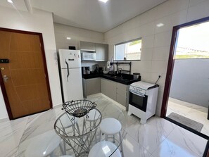 A compact kitchen with a refrigerator, microwave, stove, and a small dining area with stools.