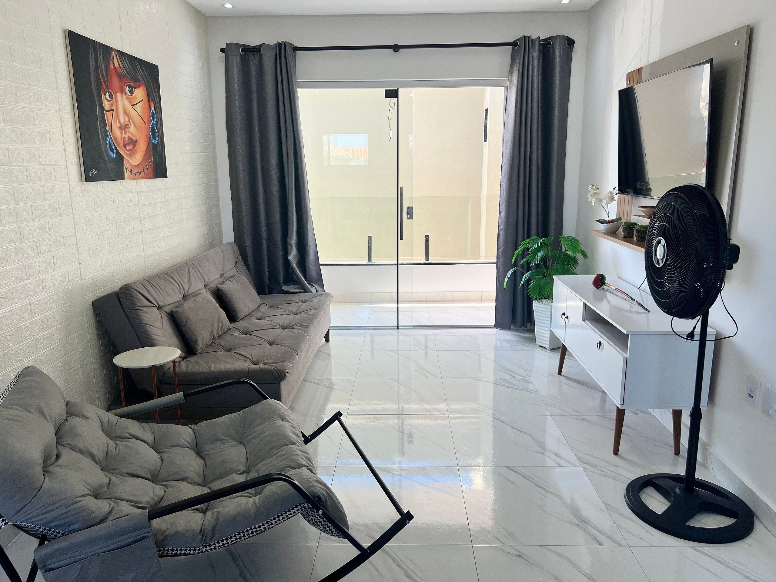 A modern living room with a grey sofa, a small round table, a white cabinet, a large mirror, and a black fan.