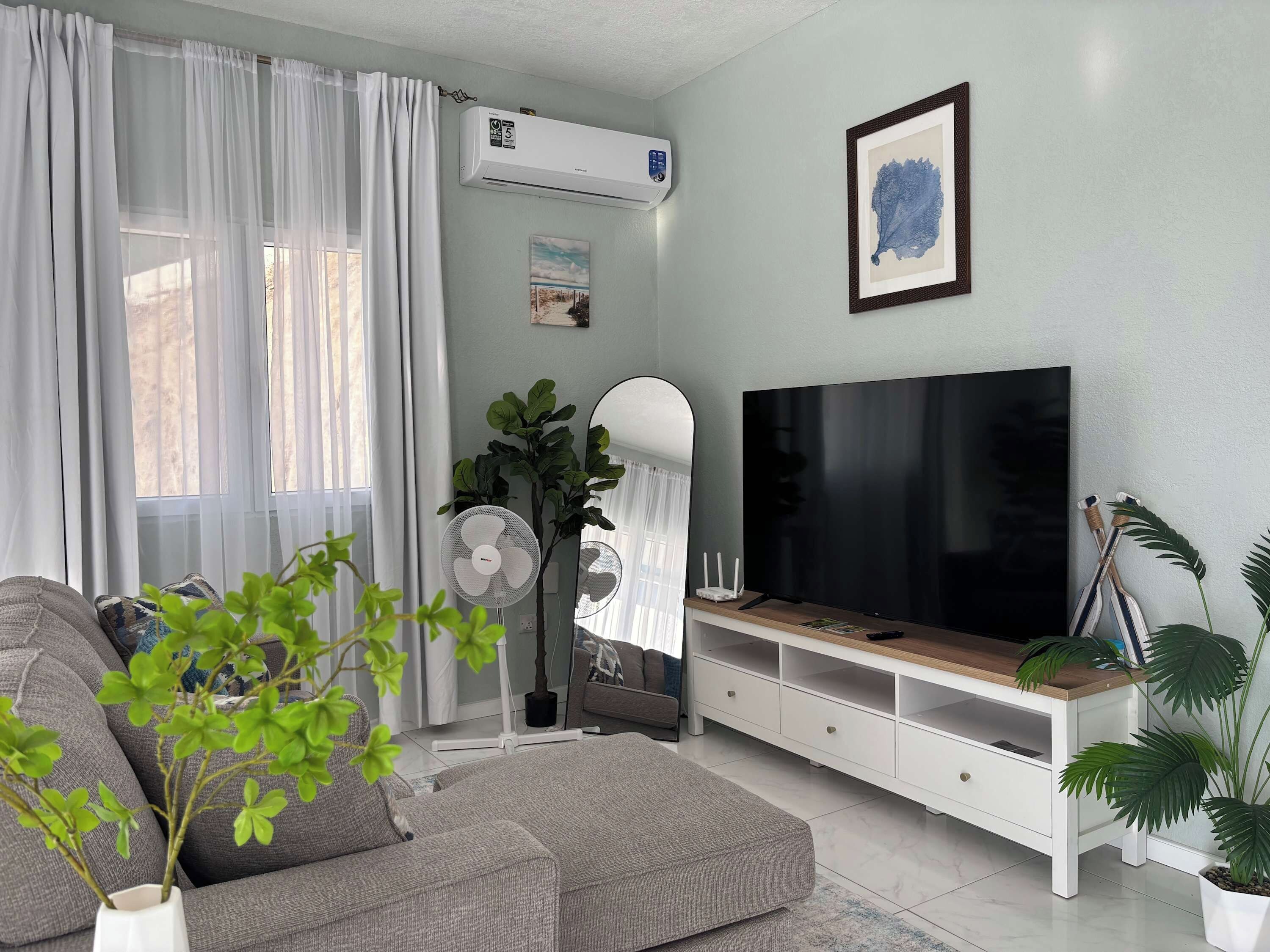 A living room with a sofa, TV, white cabinet, air conditioning unit, and potted plants.