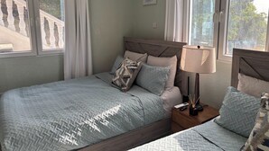 Een slaapkamer met een bed, nachtkastje, lamp en uitzicht op een trap en groen buiten.
