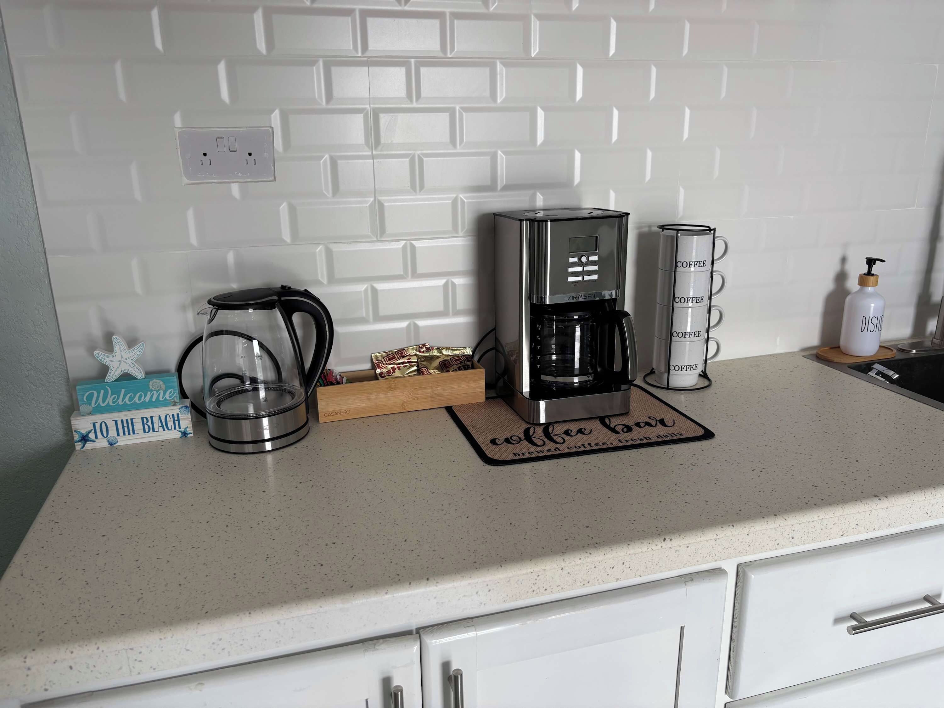 Un piano di lavoro in cucina con una macchina da caffè, un bollitore e un erogatore di caffè.