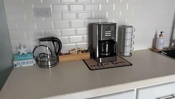 Un piano di lavoro in cucina con una macchina da caffè, un bollitore e un erogatore di caffè.