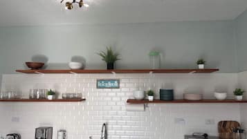 A kitchen with white brick backsplash, wooden shelves, a coffee maker, a microwave, and a blender.