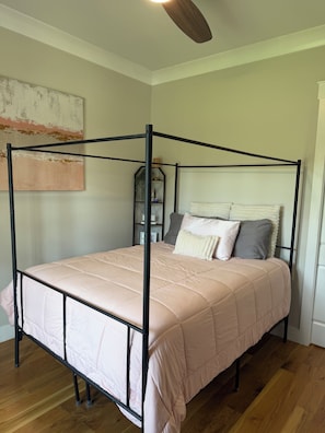 A four-poster bed with a beige quilt, a wooden floor, and a ceiling fan.