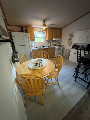 A compact kitchen with a dining area, wooden chairs, a microwave, and a refrigerator. - Newly renovated 3-bedroom mobile home in beautiful Louisa. (Louisa)