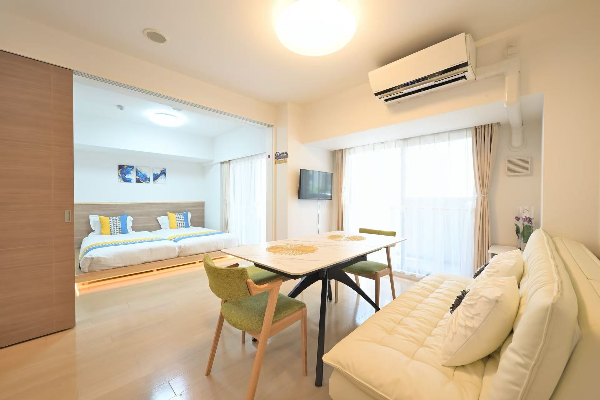 A hotel room with a bed, a dining table with chairs, a sofa, an air conditioning unit, and a television.