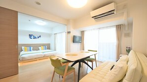 Quarto de hotel com cama, mesa de jantar com cadeiras, sofá, aparelho de ar condicionado e televisão.