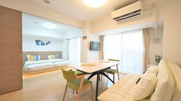 A hotel room with a bed, a dining table with chairs, a sofa, an air conditioning unit, and a television.