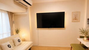 Uma sala de estar com sofá, TV de tela plana na parede, tapete redondo e mesa de jantar com banco.