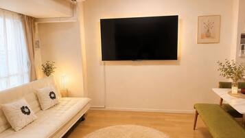 A living room with a sofa, a flat-screen TV mounted on the wall, a round rug, and a dining table with a bench.